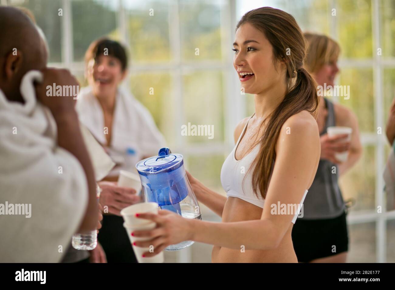 Femme adulte moyenne tenant un pichet d'eau pour verser de l'eau pour les participants après une classe d'exercice Banque D'Images