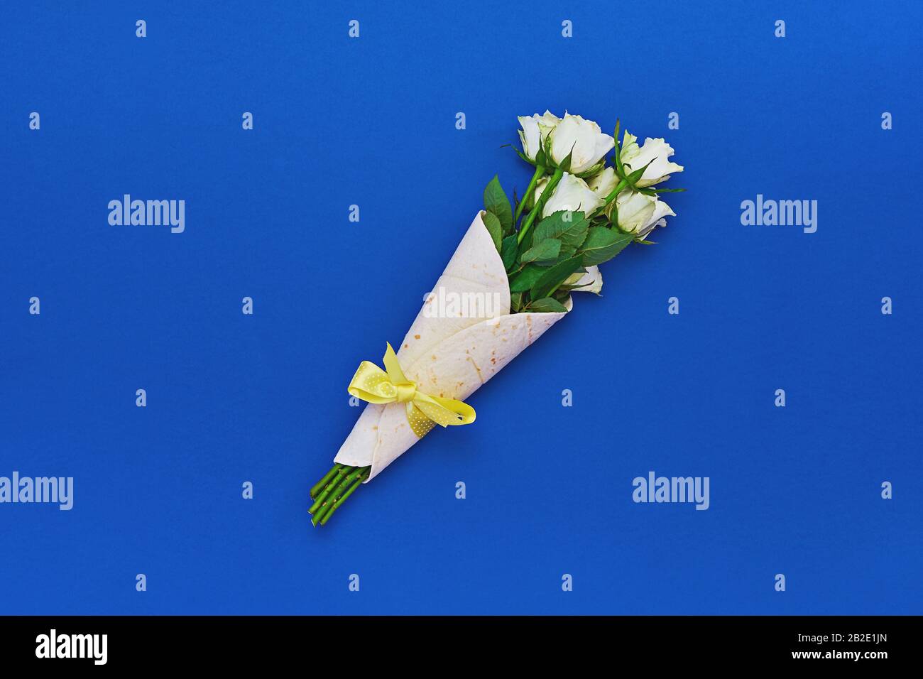 Bouquet de roses blanches enveloppées dans de la tortilla sur fond bleu classique. Concept de conditionnement de cadeaux comestibles, sans déchets ou écologique Banque D'Images