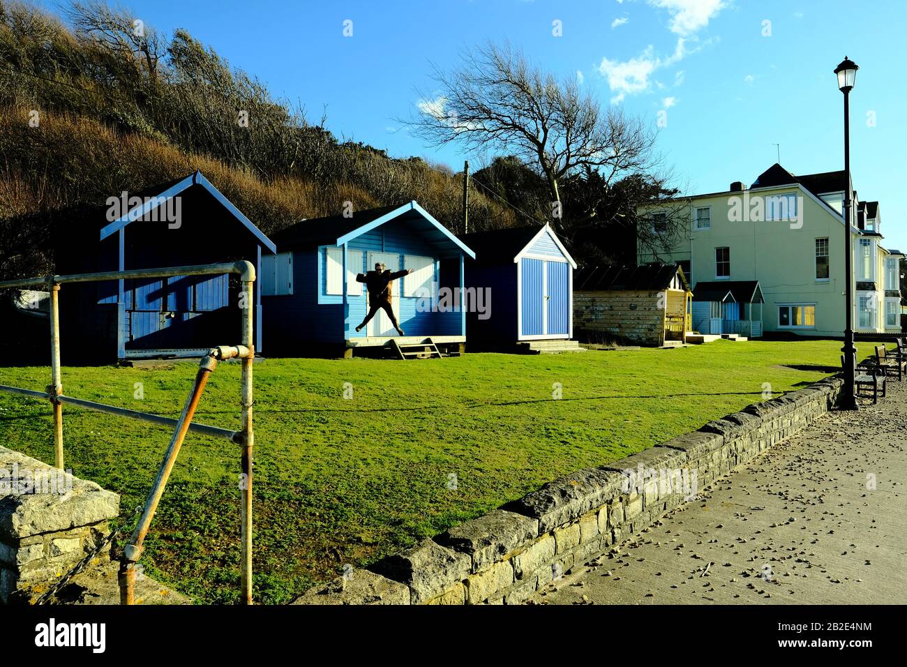Une femme sautant pour la joie du porche d'une cabane colorée sur la côte de l'île de Wight à Totland Bay Banque D'Images