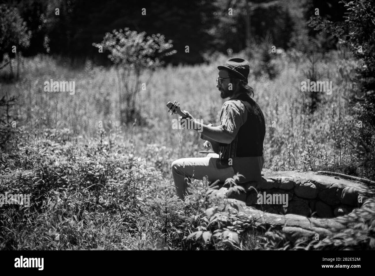 Gros plan d'un homme assis sur la pierre et jouant un instrument de musique unique appelé merlin. Photo en noir et blanc de l'artiste Banque D'Images