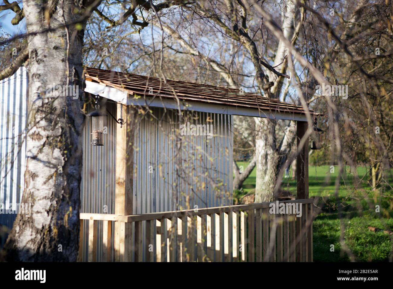 Un hangar de stockage en métal ondulé, avec une véranda en bois et un mangeoire à oiseaux et entouré d'arbres, dans un jardin communautaire Banque D'Images