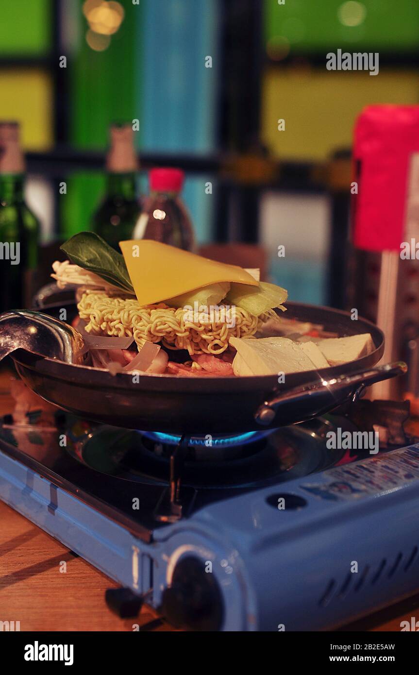 Plat cru asiatique cuit sur un four à gaz fixe - nouilles lyophilisées, une tranche de fromage et de viande dans le processus de cuisson Banque D'Images