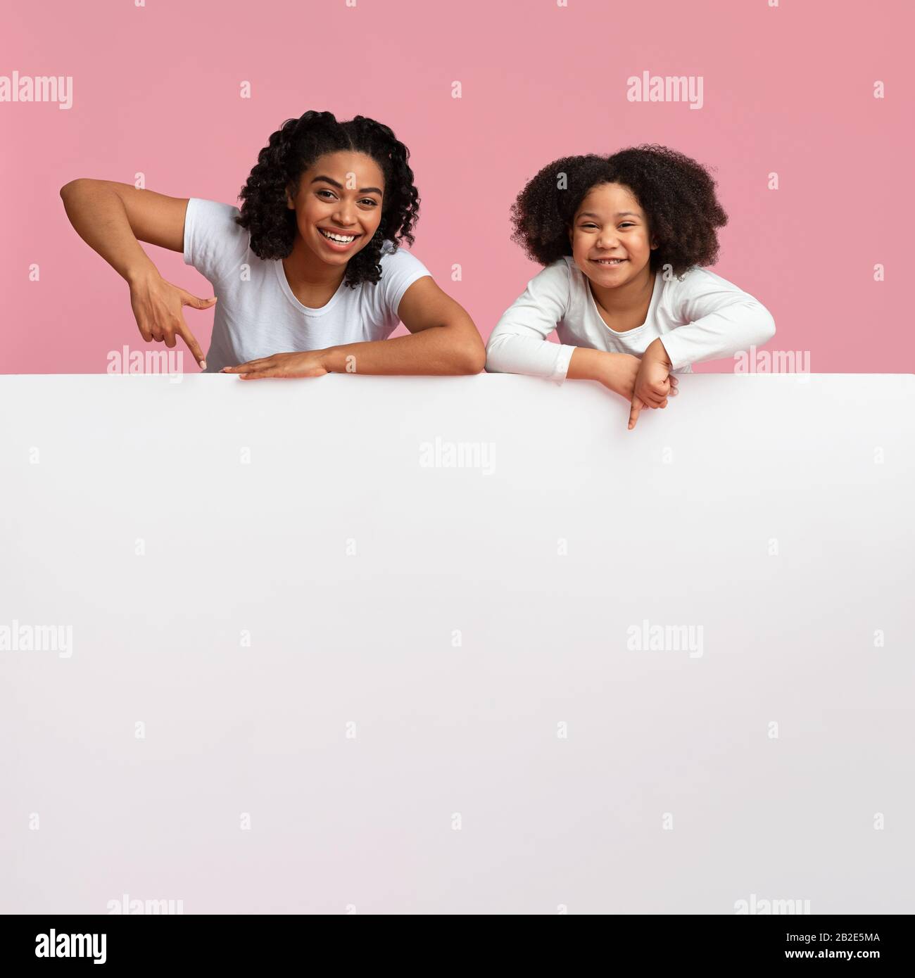 Bonne Afro Maman Et Fille Pointant Vers Le White Publicité Board Banque D'Images