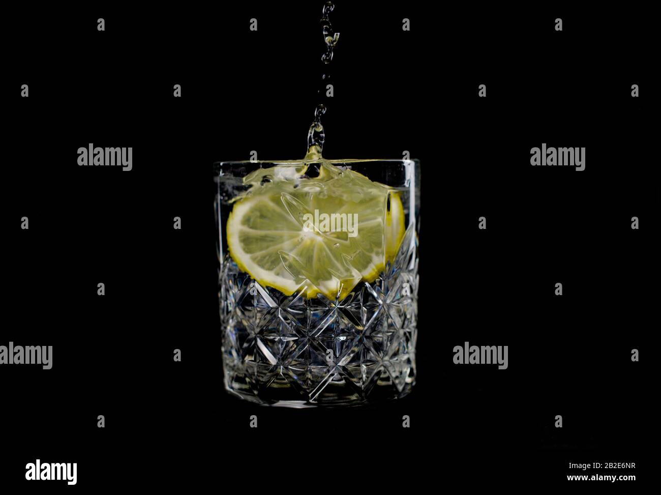 boire de l'eau avec des éclaboussures de soda de citron lorsque de la glace est projetée avec des gouttes sur un fond noir Banque D'Images