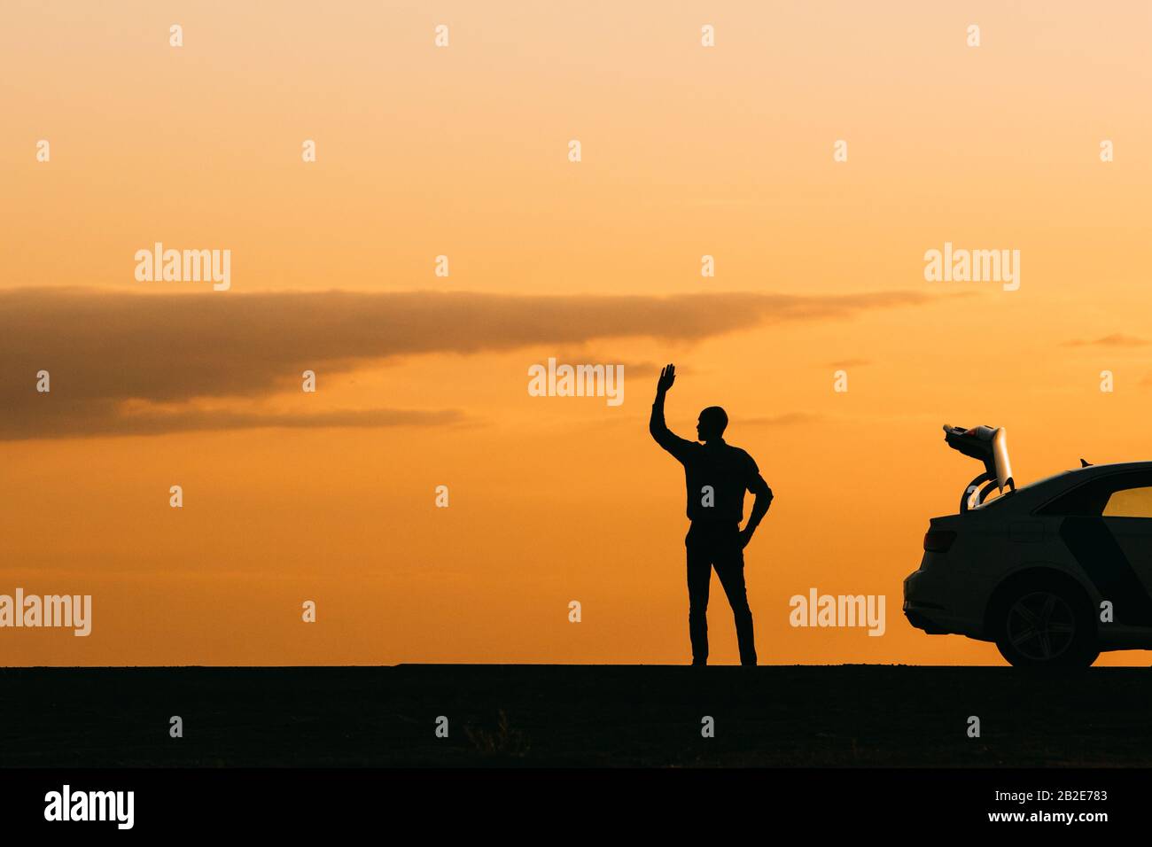 Le conducteur masculin a levé la main et attend de l'aide, sa voiture ne peut pas aller plus loin après une panne au coucher du soleil, vue latérale, espace de copie. Votes sur la route Banque D'Images