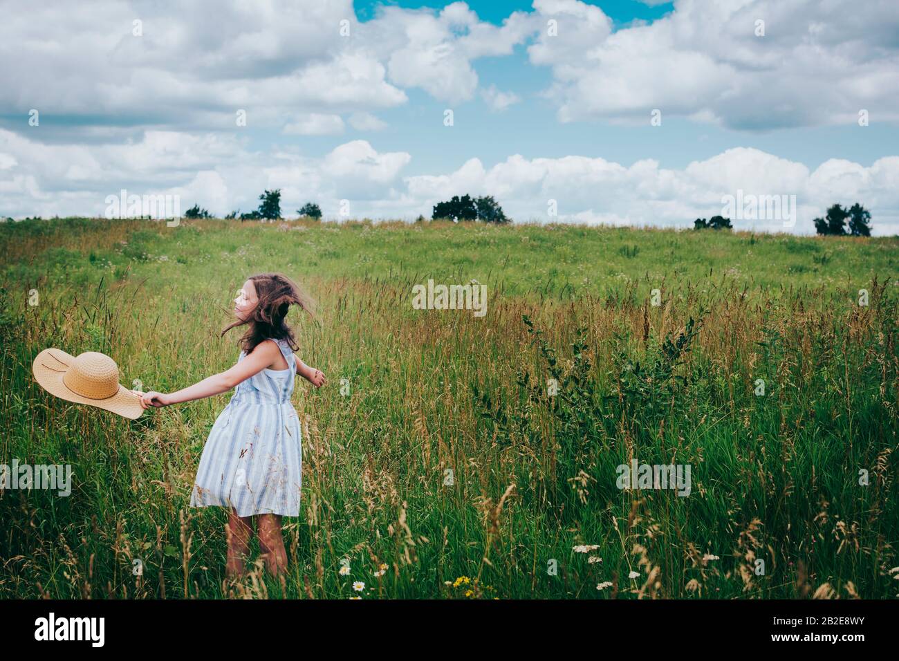 Ten Girl Twirling dans un Grassy Field lors d'une journée d'été nuageuse Banque D'Images