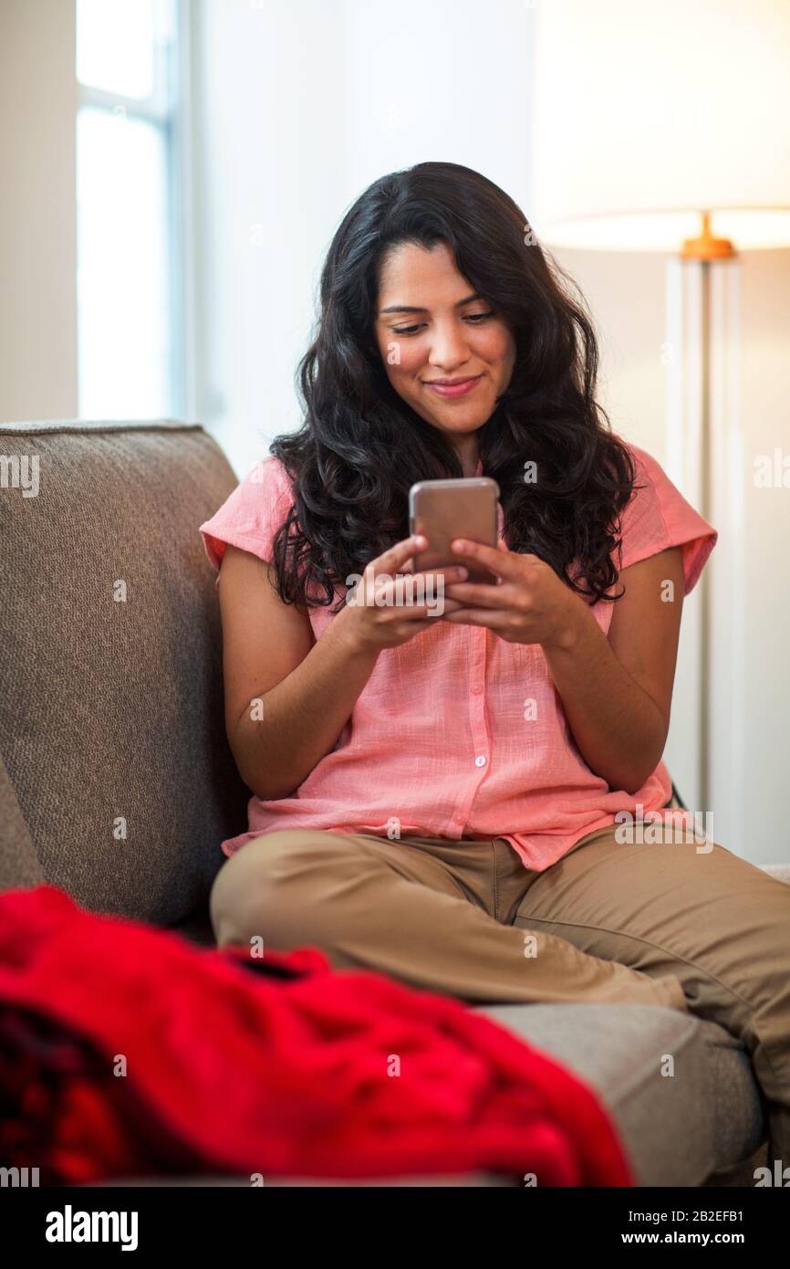 Femme hispanique souriante utilisant son téléphone à la maison. Banque D'Images