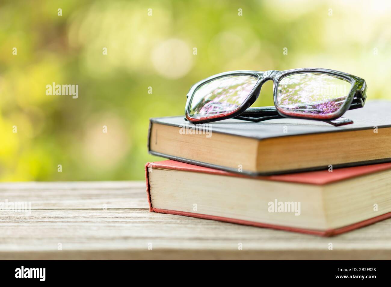 Gros livre et lunettes de vue sur table en bois avec fond de flou vert abstrait. Concept de lecture et d'éducation Banque D'Images