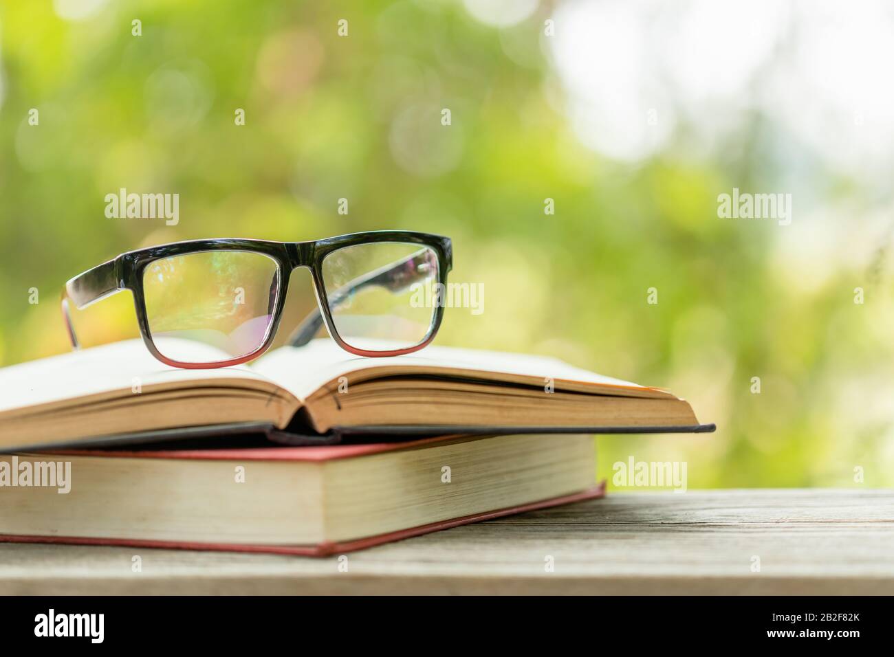 Gros livre et lunettes de vue sur table en bois avec fond de flou vert abstrait. Concept de lecture et d'éducation Banque D'Images
