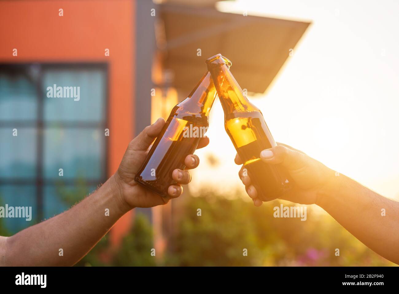 Fermez deux personnes tenant la bouteille de bière et célébrez à l'extérieur de la maison. Déménagement à la maison ou bâtiment de maison terminé concept Banque D'Images