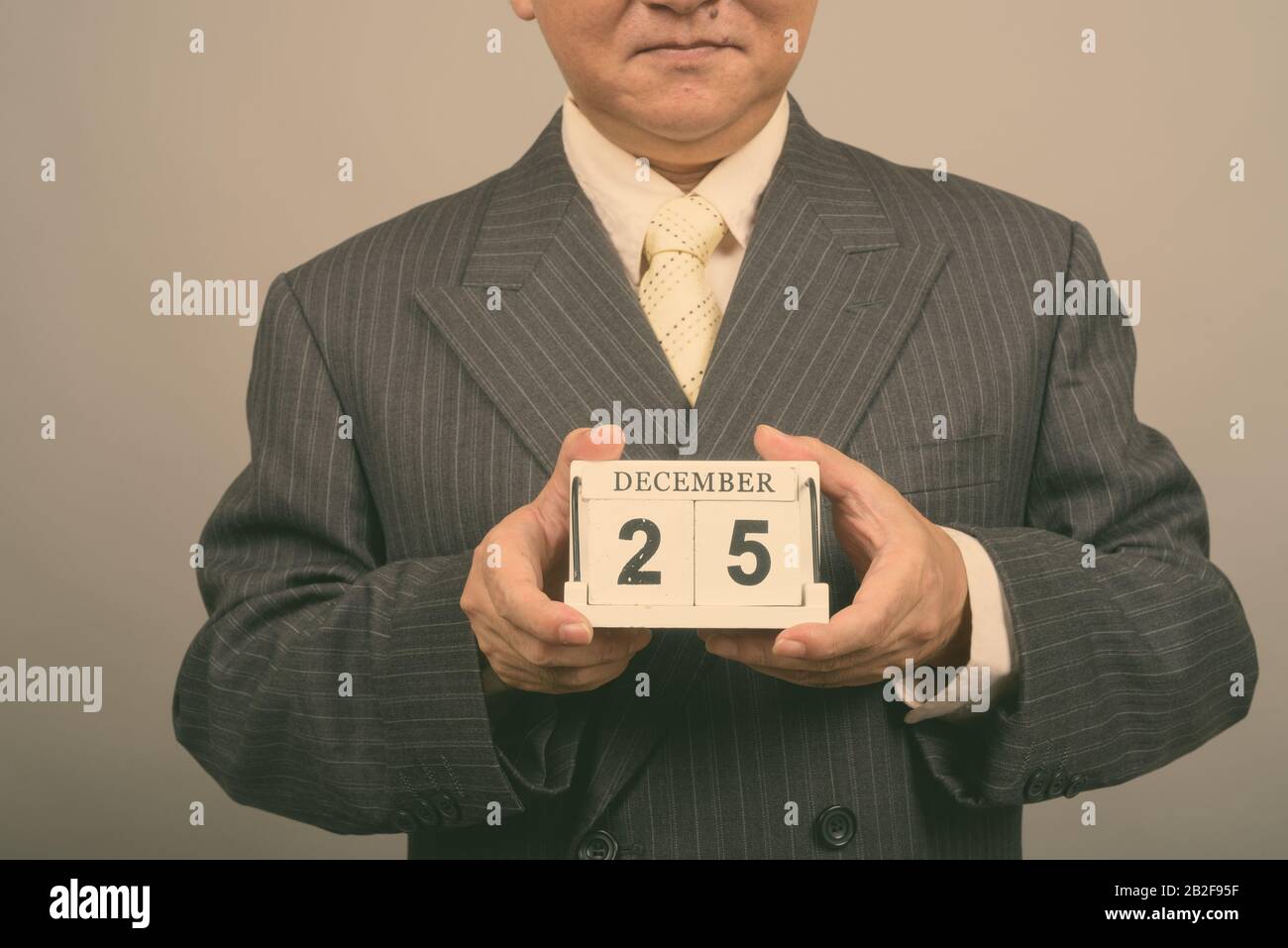 Studio tiré des mains d'un homme d'affaires asiatique mûr tenant des blocs calendrier prêts pour Noël contre fond gris Banque D'Images