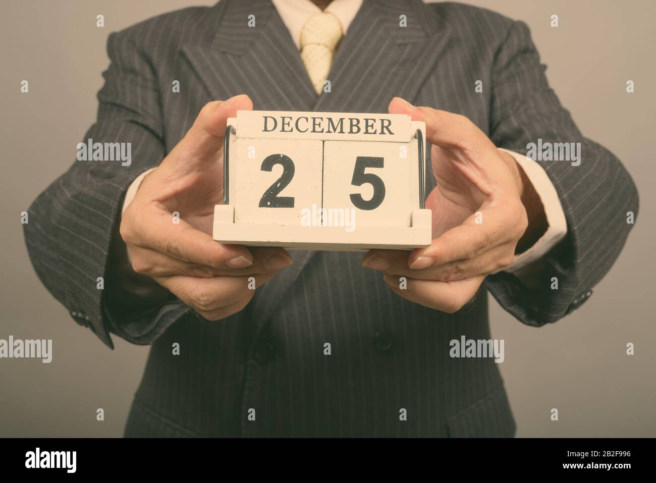 Studio tiré des mains d'un homme d'affaires asiatique mûr tenant des blocs calendrier prêts pour Noël contre fond gris Banque D'Images