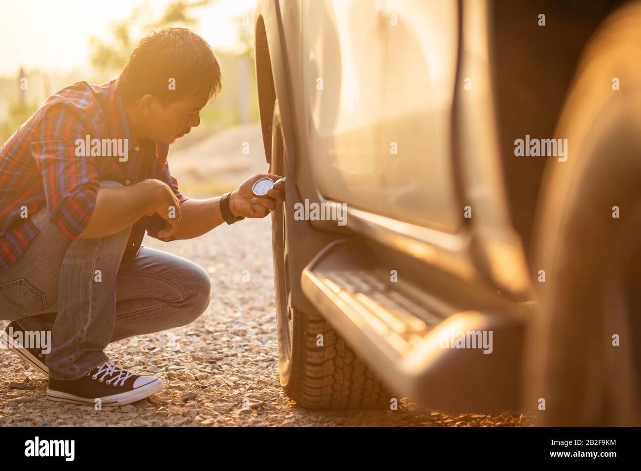 Homme asiatique qui contrôle la pression d'air et remplit l'air dans les pneus de sa voiture. Entretien de la voiture avant la conduite concept Banque D'Images