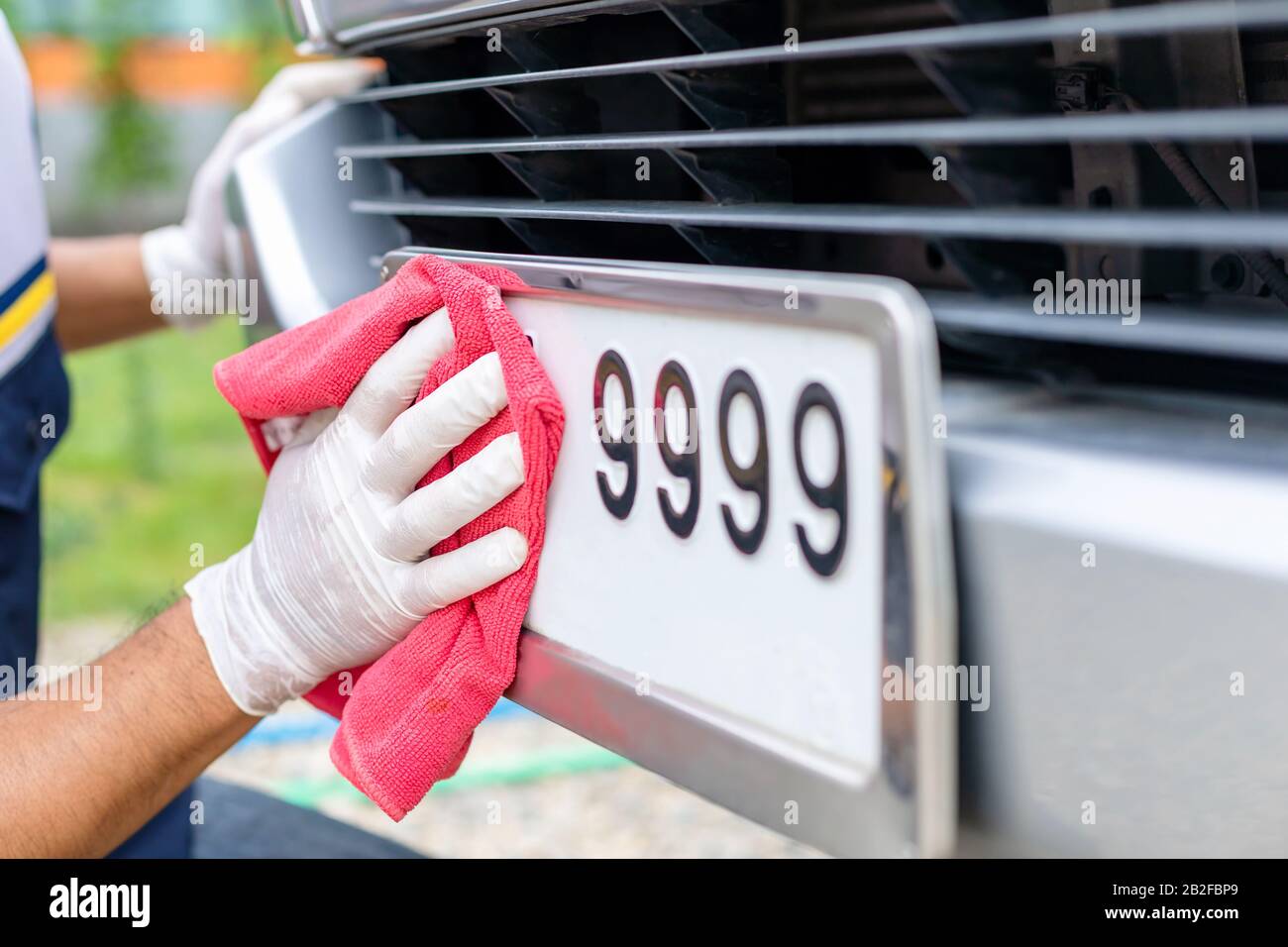 Homme utilisant un chiffon rouge pour nettoyer la plaque avant de voiture numéro. Concept de voiture de nettoyage Banque D'Images