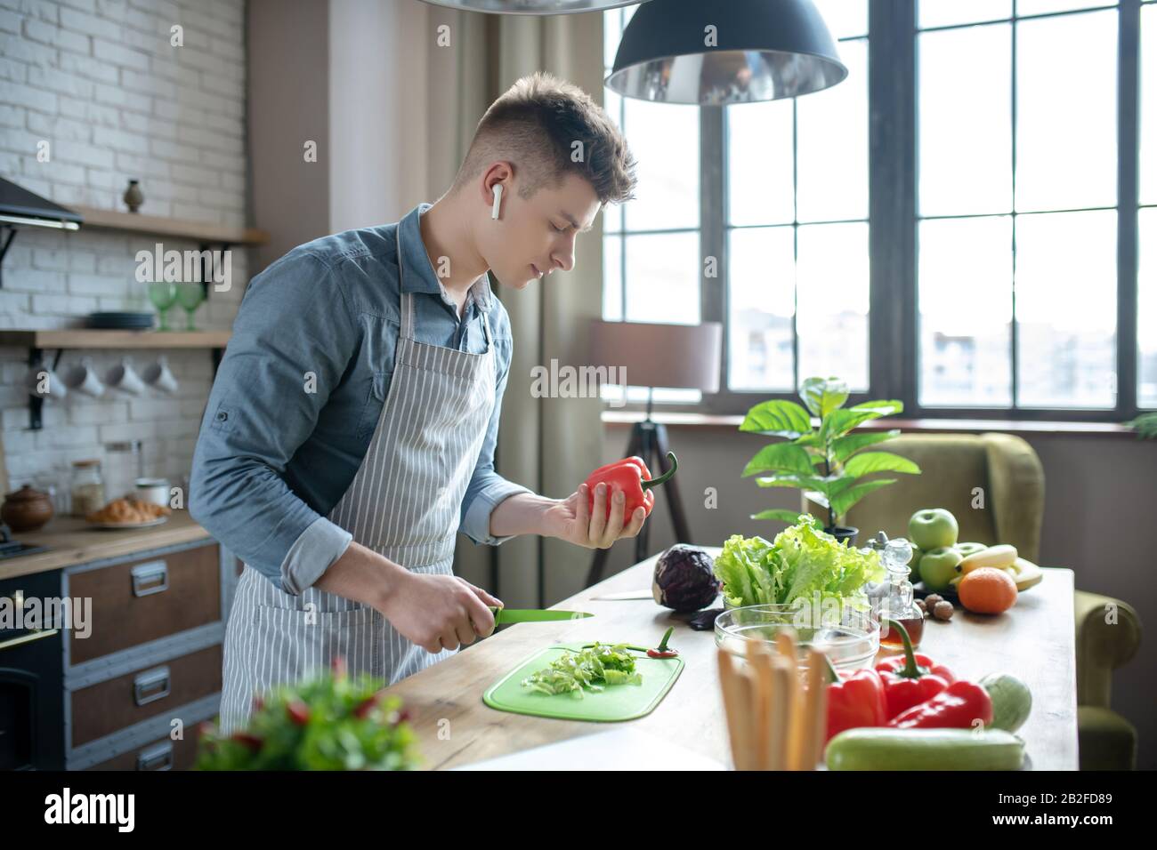 Un jeune homme qui a réussi à trancher des légumes frais dans la cuisine. Banque D'Images