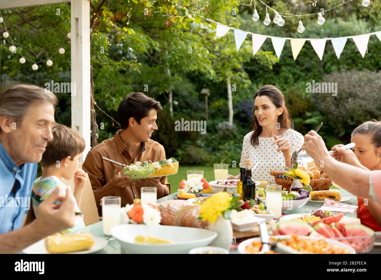 Vue de face d'une famille caucasienne de plusieurs générations assise à l'extérieur d'une table de dîner pour un repas, manger, parler et servir les uns les autres. Le Famil Banque D'Images