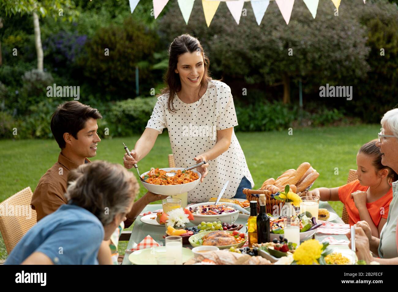Vue de face d'une famille caucasienne de plusieurs générations assise à l'extérieur d'une table de dîner pour un repas, parler et servir de la nourriture. Famille profitant du temps à Banque D'Images