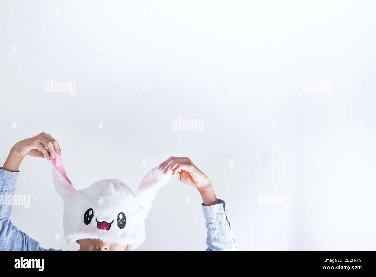 Un garçon tient les mains oreilles chapeau Kawaii Rabbit sur un fond clair, concept de Pâques Banque D'Images