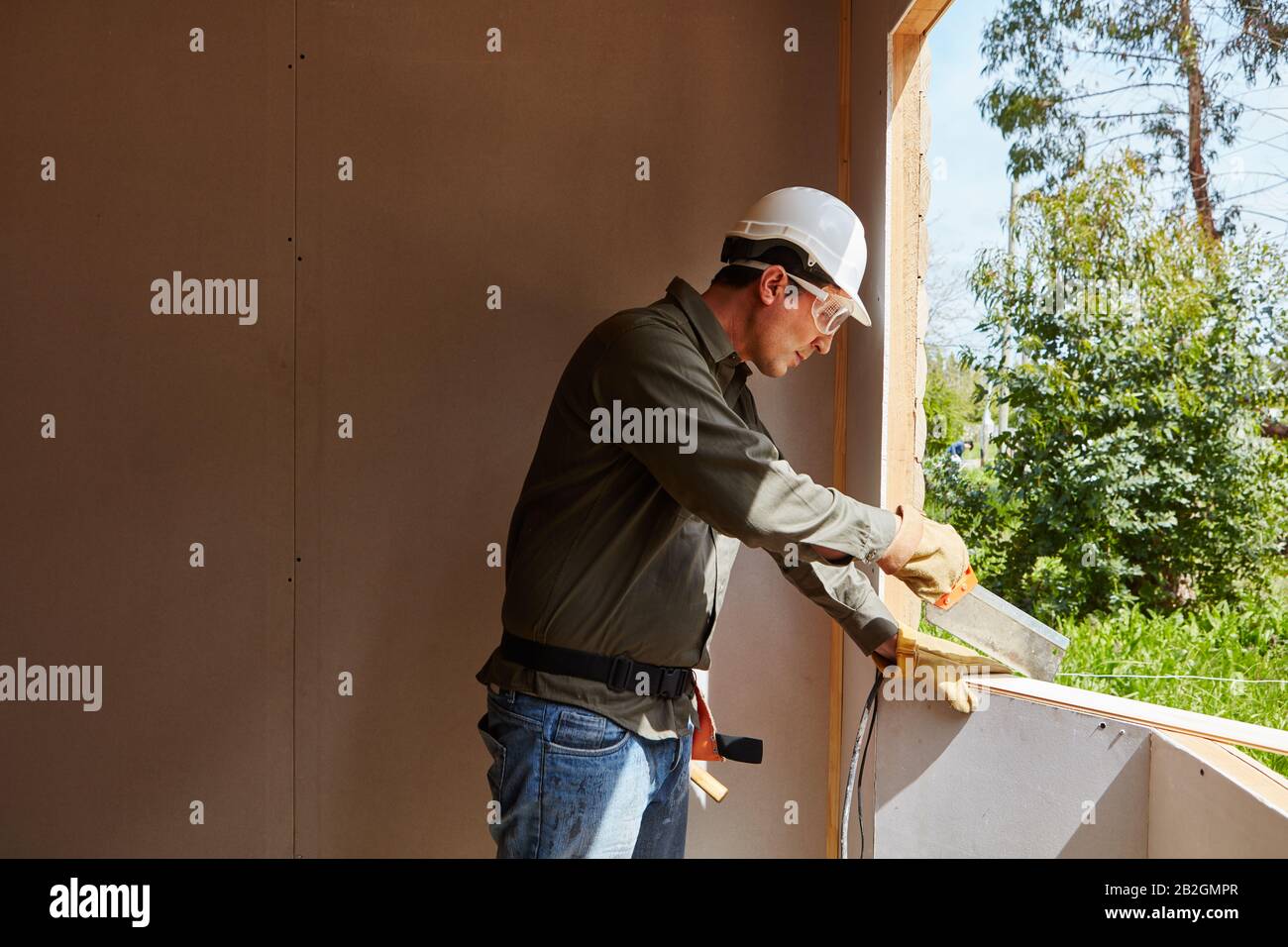 Artisan avec scie et vêtements de protection lors de la construction d'une maison Banque D'Images