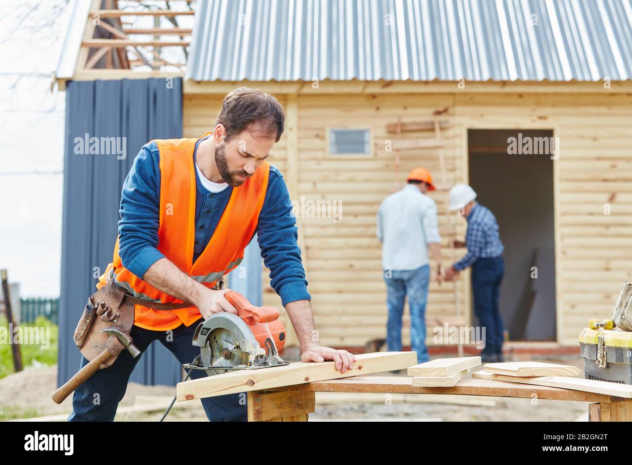 Artisan avec scie circulaire pendant la construction d'une maison en face d'une maison sur le chantier Banque D'Images