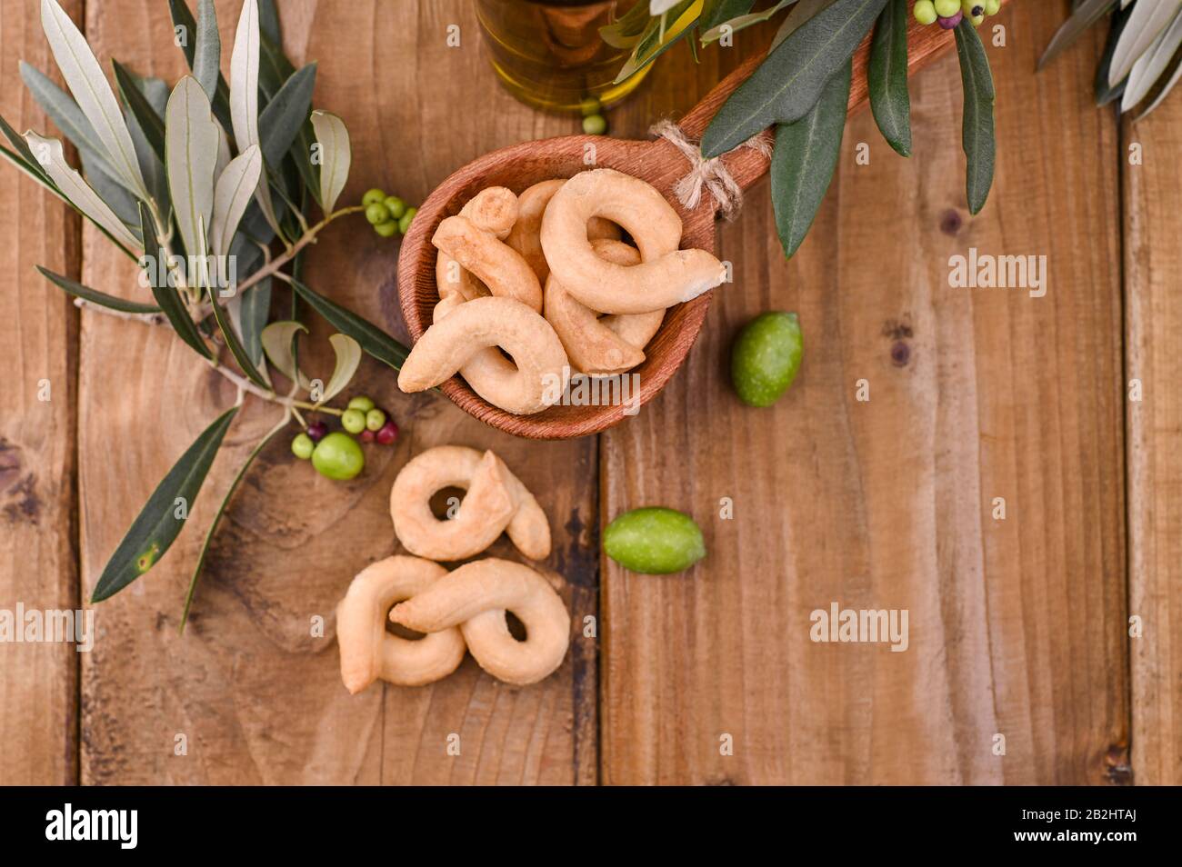 Le taralli est un snack-restaurant italien traditionnel typique de la cuisine régionale des Pouilles. Tarallini avec branches d'olive fraîches sur une table en bois. Espace de copie. Ci-Dessus. Banque D'Images