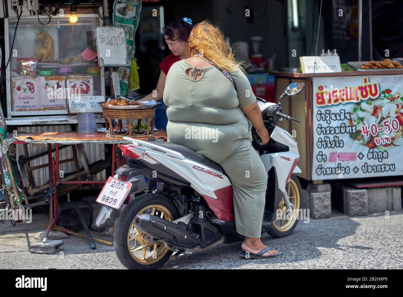 Une femme obèse sur une moto qui collecte la nourriture d'un stand de nourriture de rue. Thaïlande Asie Du Sud-Est Banque D'Images