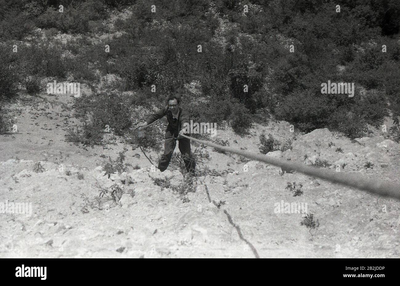 Années 1950, historique, homme qui s'enfuit dans une falaise rocheuse, Angleterre, Royaume-Uni. La technique consiste à utiliser votre corps et la corde pour faire une descente contrôlée, en utilisant vos pieds et vos jambes comme soutien et équilibre lorsque vous vous abaissez. À cet égard, il les compétences physiques et mentales nécessaires pour descendre en rappel, a vu devenir un «sport d'aventure» populaire ou «activité de plein air». Banque D'Images