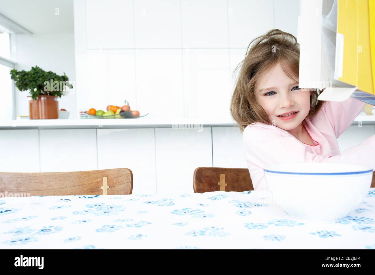 Fille (5-6) assise à la table avec bol et boîte de céréales Banque D'Images