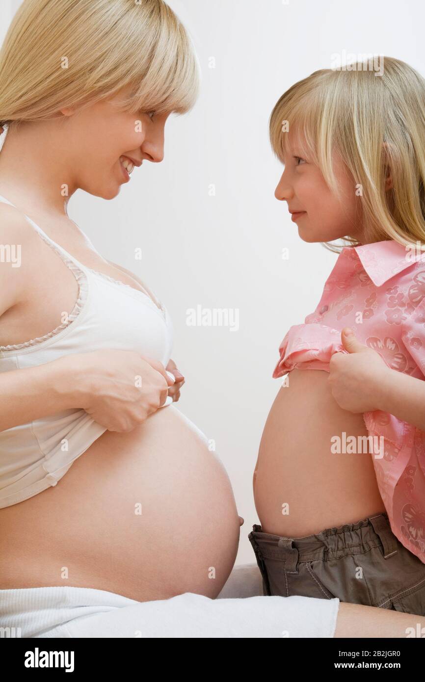 Fille (7-9) et mère enceinte montrant des abdomens l'un à l'autre Banque D'Images