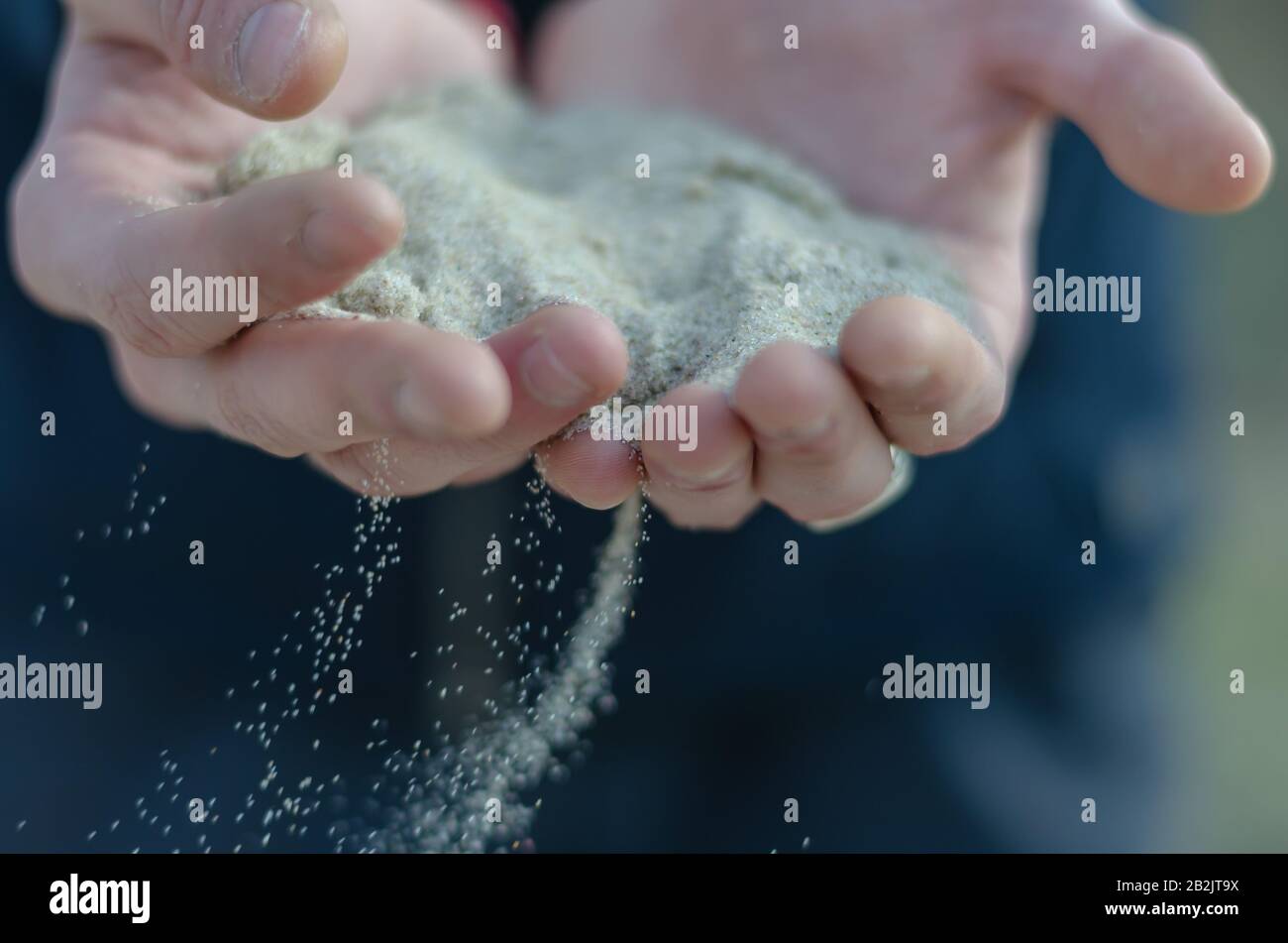 Le sable coule à travers les doigts. Les grains blancs de sable proviennent d'une poignée de jeunes hommes. Le concept de temps de course à pied. Mise au point sélective. Gros plan. Banque D'Images