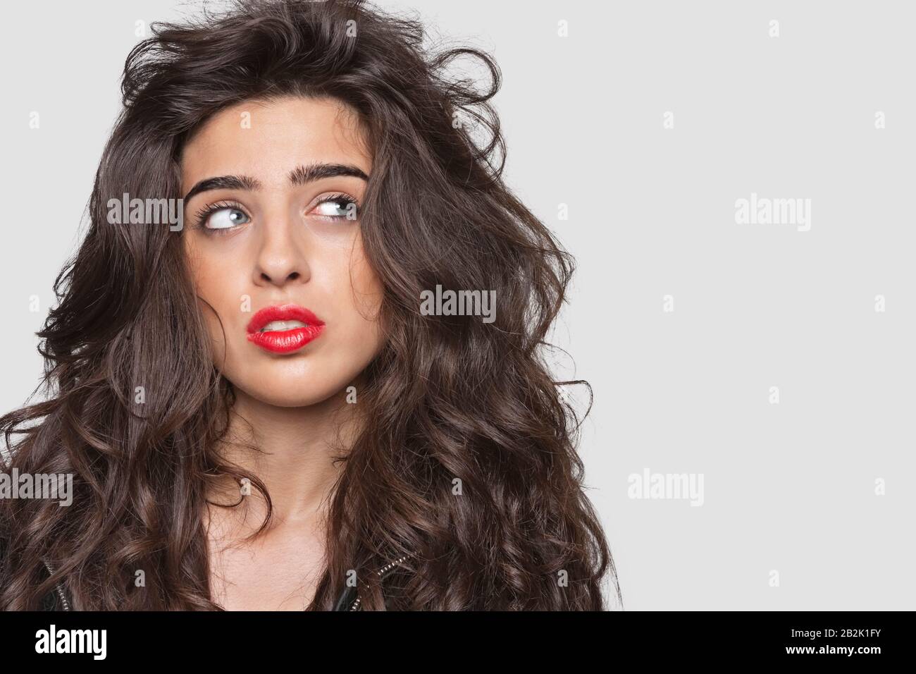 Jeune femme pensive avec lèvres rouges regardant latéralement sur fond gris Banque D'Images