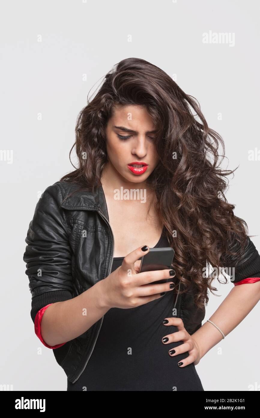 Jeune femme pensive utilisant le téléphone cellulaire sur fond gris Banque D'Images