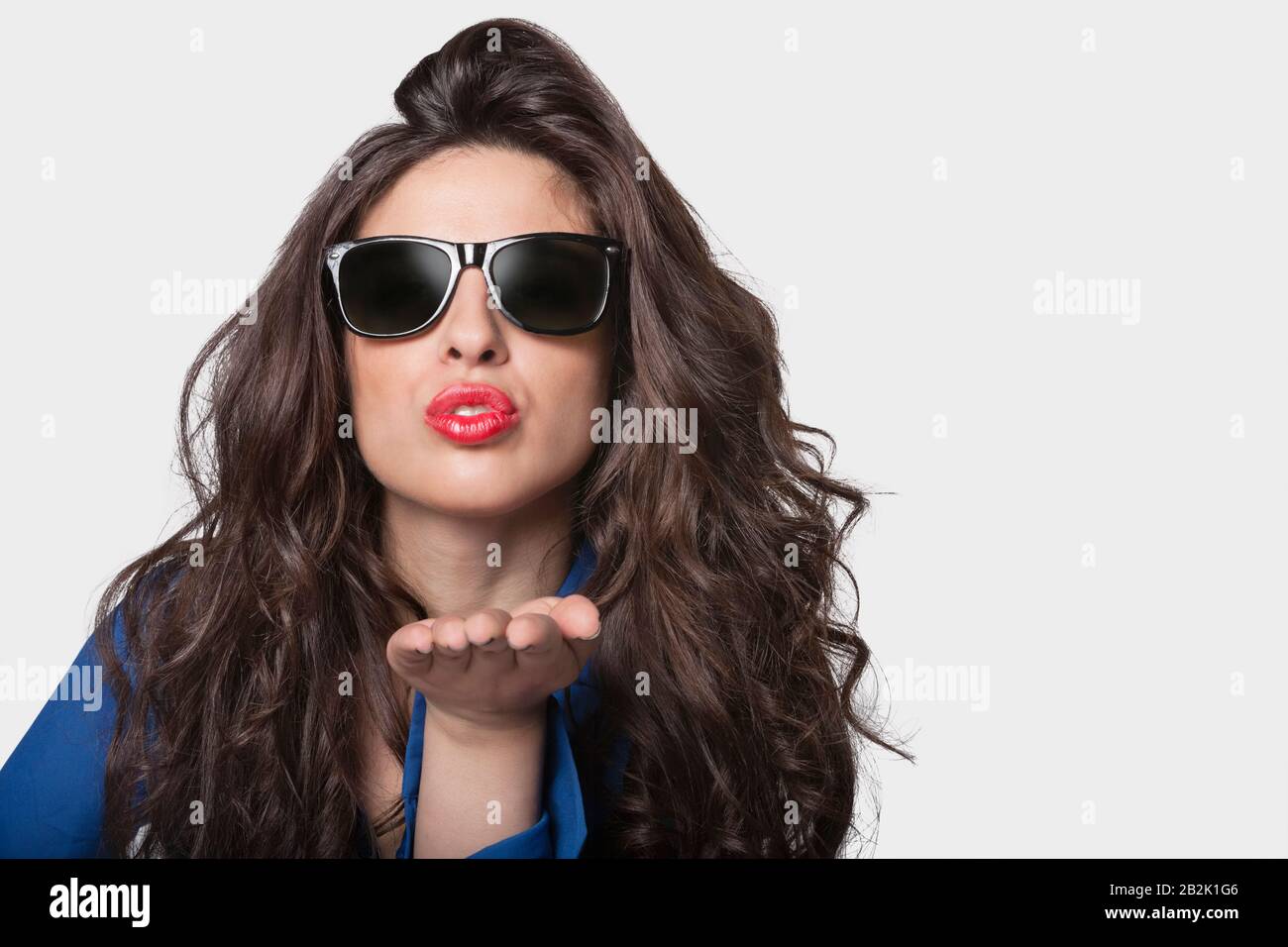 Portrait d'une jeune femme dans des lunettes de soleil soufflant un baiser sur fond gris Banque D'Images