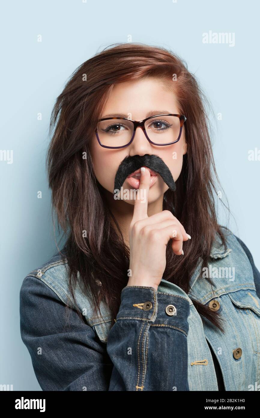 Portrait de la jeune femme avec une fausse moustache et doigt sur ses lèvres sur fond bleu clair Banque D'Images