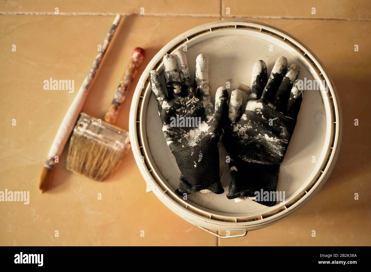 Peinture sur le sol après utilisation. Peindre des gants, une casserole et des brosses avec de la peinture blanche au milieu d'une maison en construction. Banque D'Images