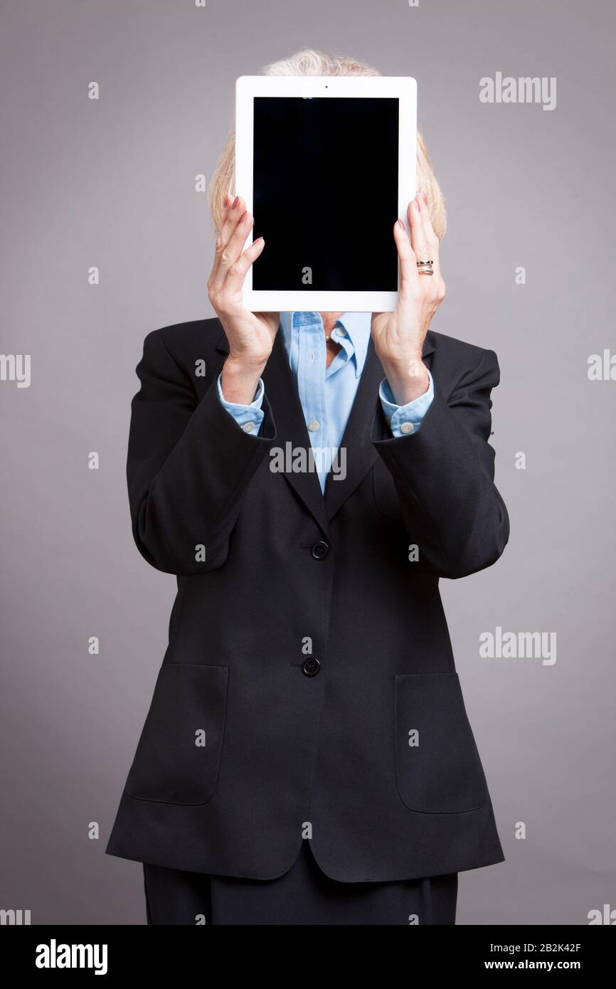 Portrait de la femme d'affaires senior qui cache son visage sur une tablette numérique sur fond gris studio Banque D'Images