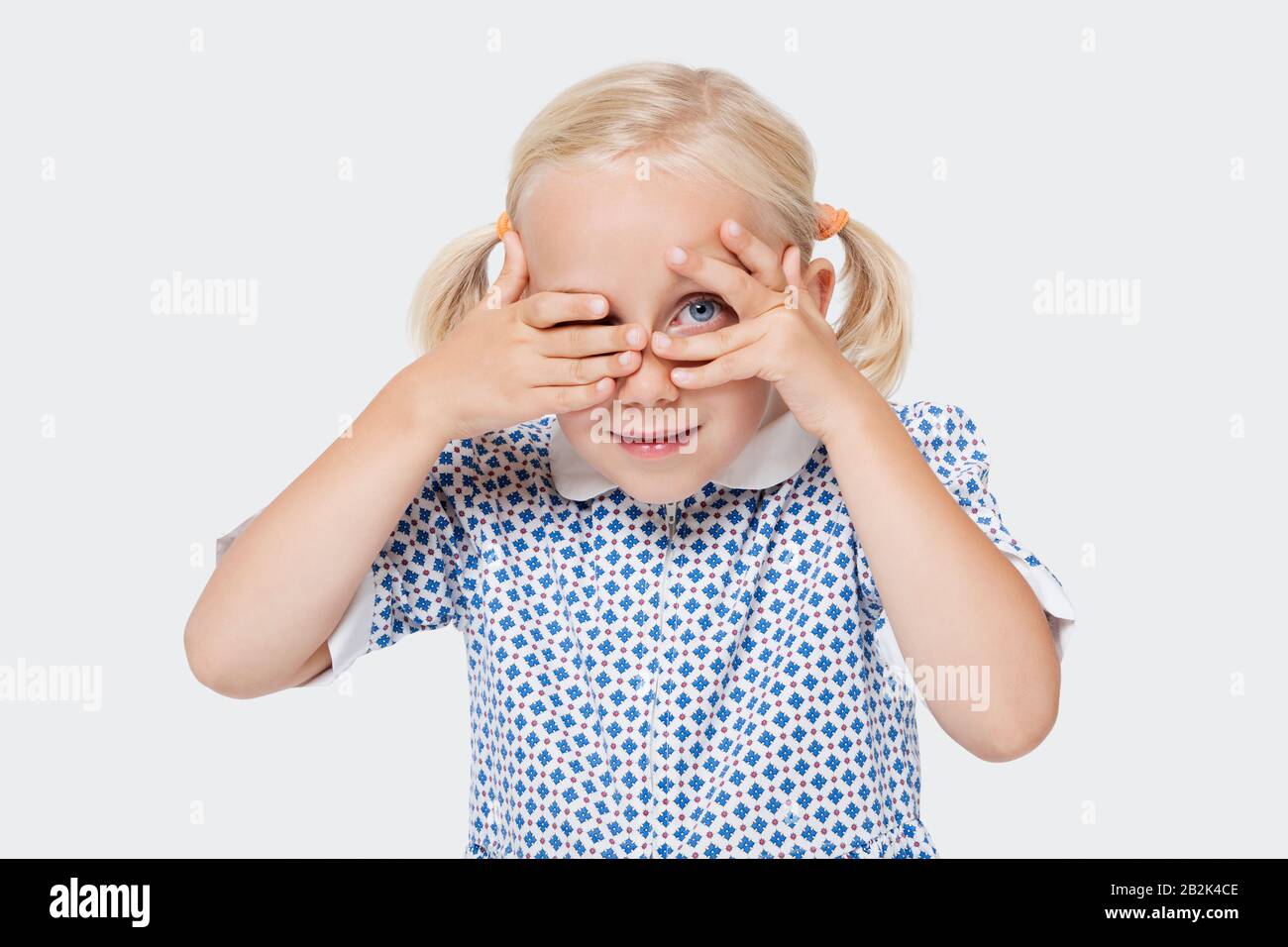 Portrait d'une jeune fille épluchant à travers les doigts sur fond blanc Banque D'Images