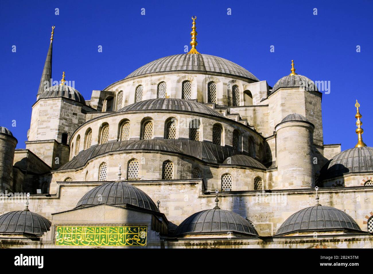 Une grande mosquée de pierre avec un grand dôme central flanqué de dômes plus petits et un grand minaret, le tout surmonté de parquets dorés. La structure comprend des fenêtres cintrées avec un treillis complexe et un Banque D'Images