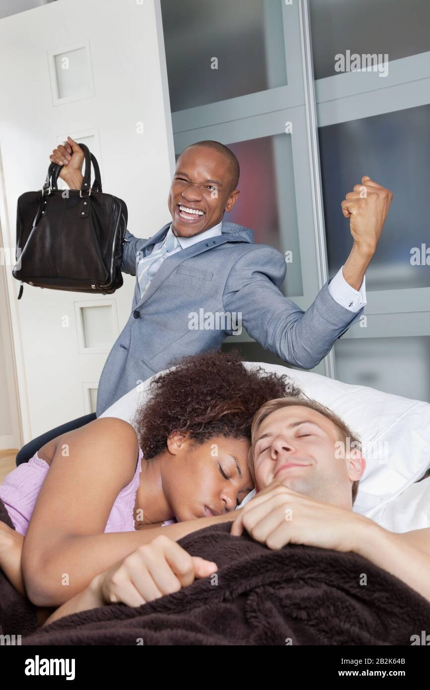 Couple multiethnique au lit avec des hommes d'affaires enthousiastes en arrière-plan Banque D'Images