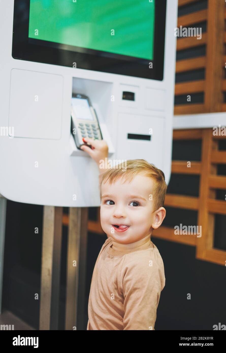 Petit mignon petit garçon enfant debout à côté de stand avec paiement électronique dans le centre commercial ou le café Banque D'Images