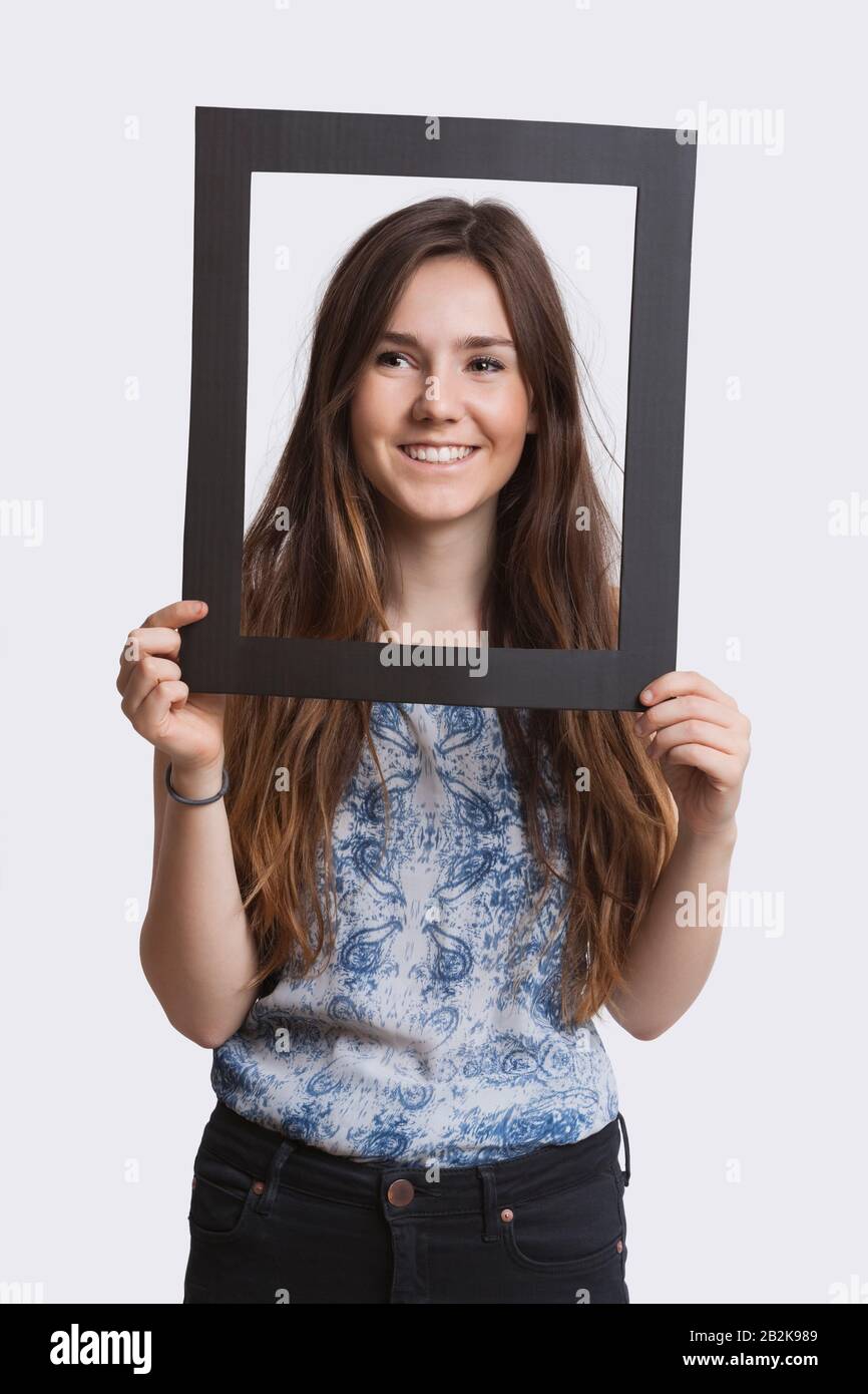 Portrait de la jeune femme souriant à travers le cadre sur fond blanc Banque D'Images
