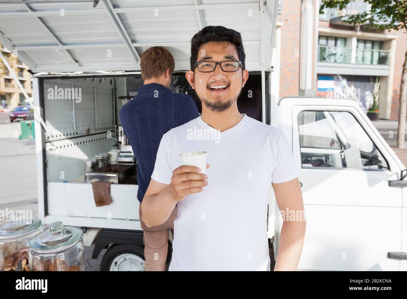 Portrait du client tenant une tasse à café jetable contre le vendeur et le magasin mobile Banque D'Images
