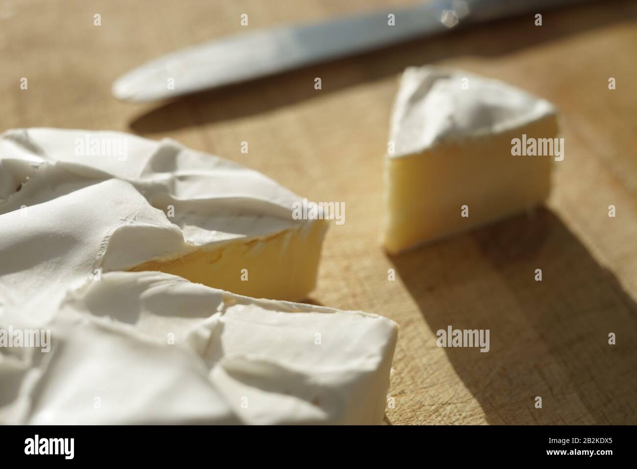 Fromage Camembert avec une tranche triangulaire et un couteau sur une planche en bois. Banque D'Images