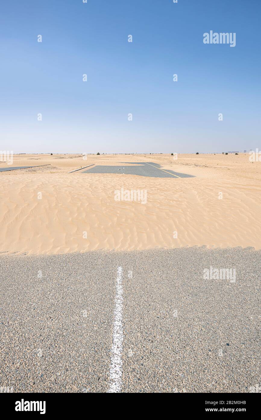 Photo verticale d'une route vide recouverte de sable dans le désert avec un grand espace de copie dans le ciel bleu Banque D'Images