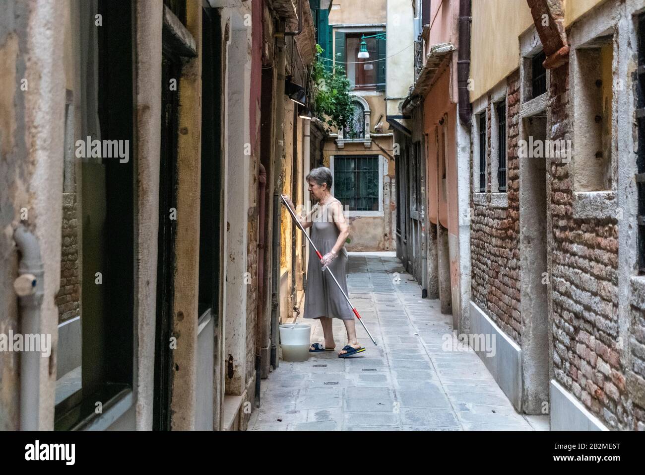 Une habitante locale nettoie ses fenêtres dans une allée étroite à Venise, en Italie Banque D'Images