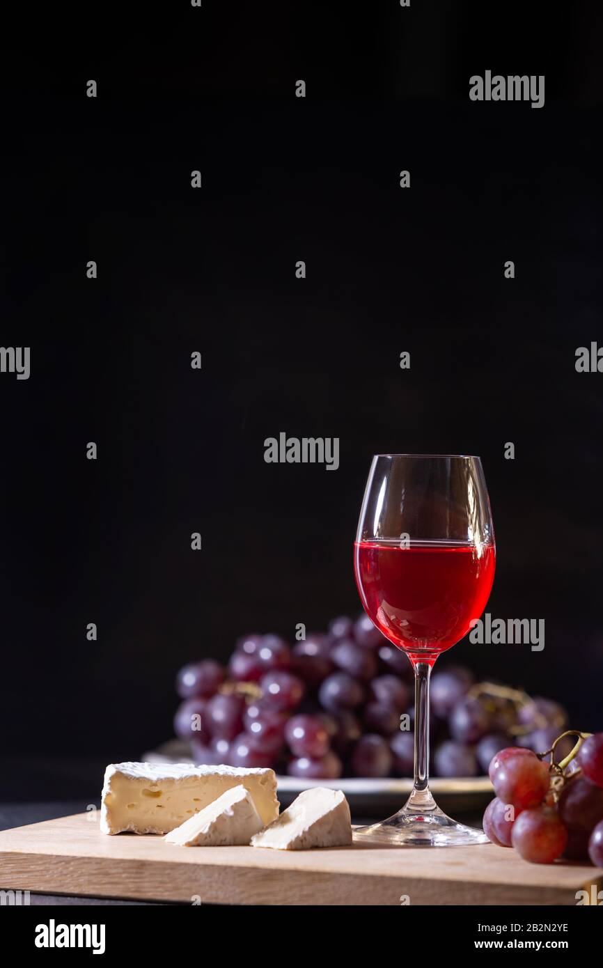 Un verre de vin de fruits rouges. Gros plan de la vigne et du fromage de brie sur un fond sombre en touche basse. Espace de copie. Bannière pour café, domaine viticole et restaurant. Banque D'Images