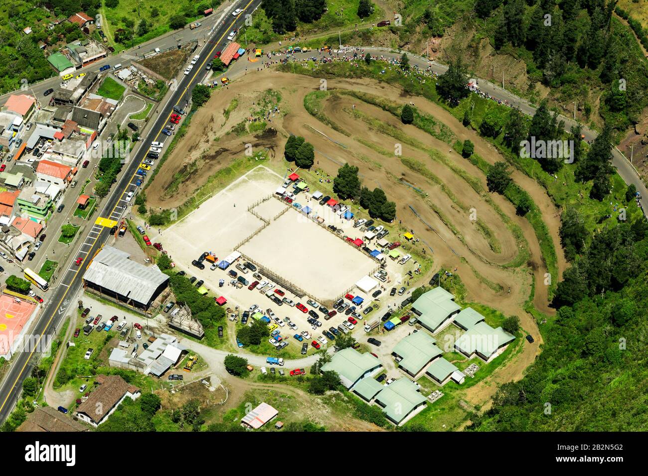 Une photographie aérienne montre une grande piste de terre avec plusieurs voies courbes, probablement pour des événements hors route ou de motocross, adjacente à une route pavée avec des véhicules. Une grande zone pavée rectangulaire, peut-être un Banque D'Images