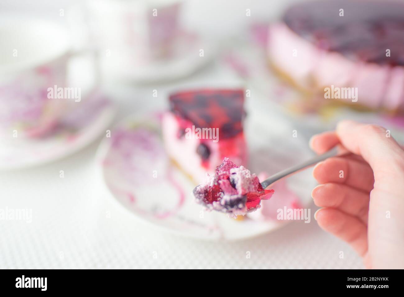 Main féminine avec cuillère et cheesecake à cassis. Soucoupe avec gâteau au fromage de cassis et cuillère sur une table blanche Banque D'Images