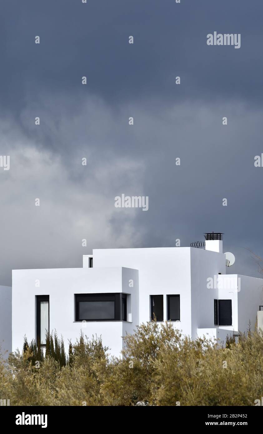 Vue sur une maison individuelle moderne et blanche, derrière des oliviers Avec des nuages sombres en arrière-plan en Andalousie Banque D'Images Vue sur une maison individuelle moderne et blanche, derrière des oliviers Avec des nuages sombres en arrière-plan en Andalousie Banque D'Images