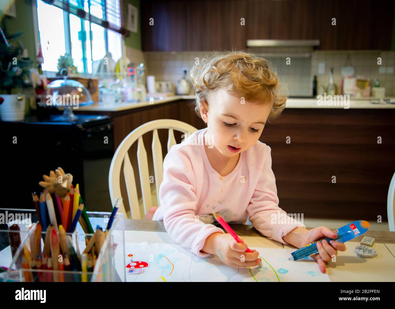 jeune fille assise à la table de cuisine coloriant dans le papier à la maison. Banque D'Images